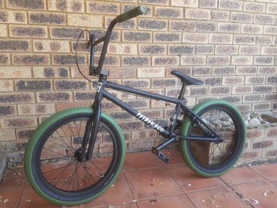 A photo of a 2019 Fit STR Complete 20 inch BMX. It is completely matt black (black frame, handle bars and wheel rims), with the exception of olive green grips and tires.